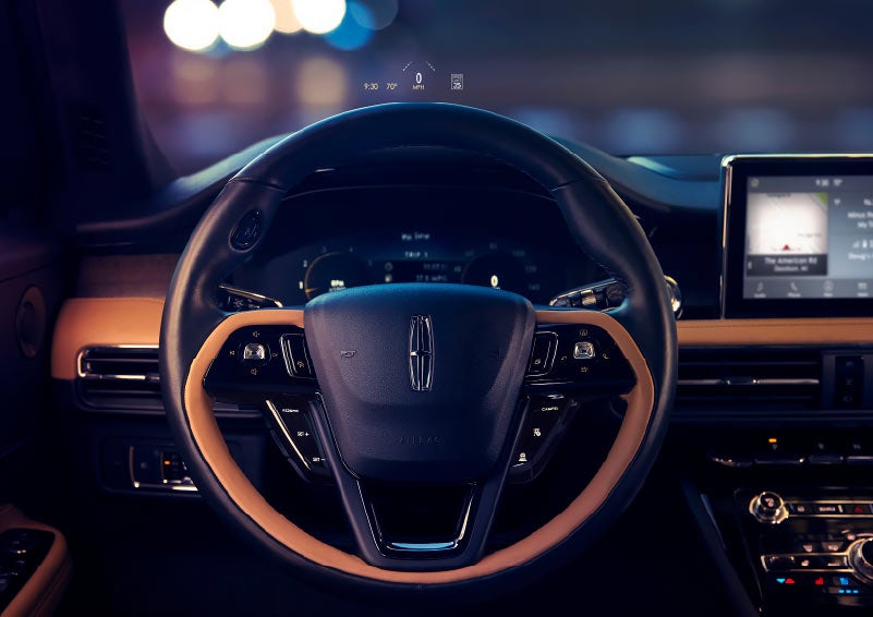 The available head up display projects data on the windshield above the steering wheel inside a 2021 Lincoln Corsair as the driver prepares to navigate the city at night